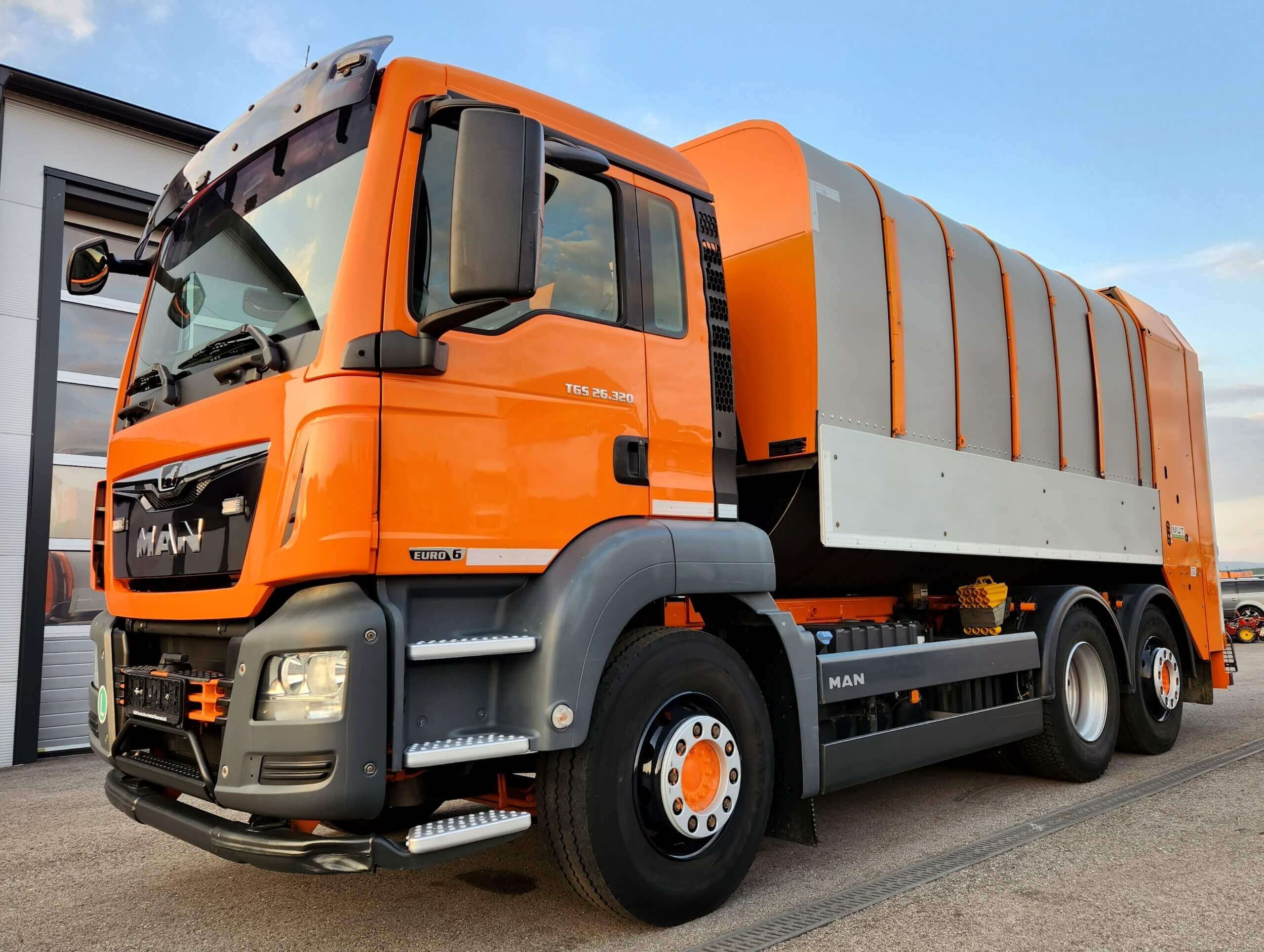 Orange Müllwagen von MAN auf einem Parkplatz bei Tageslicht. Euro 6 Modell, bereit für Abfallentsorgungseinsatz.