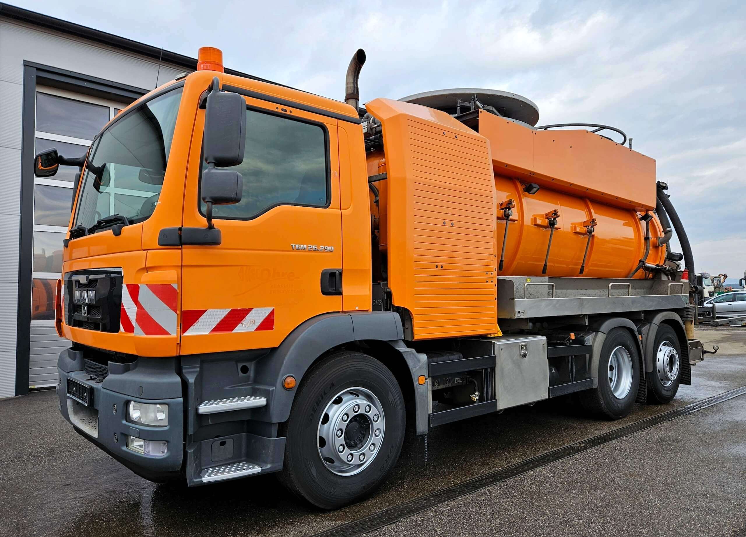 Orangefarbener LKW für Kanalreinigung, geparkt vor einem Gebäude. Hochwertiges Fahrzeug für professionelle Reinigung.