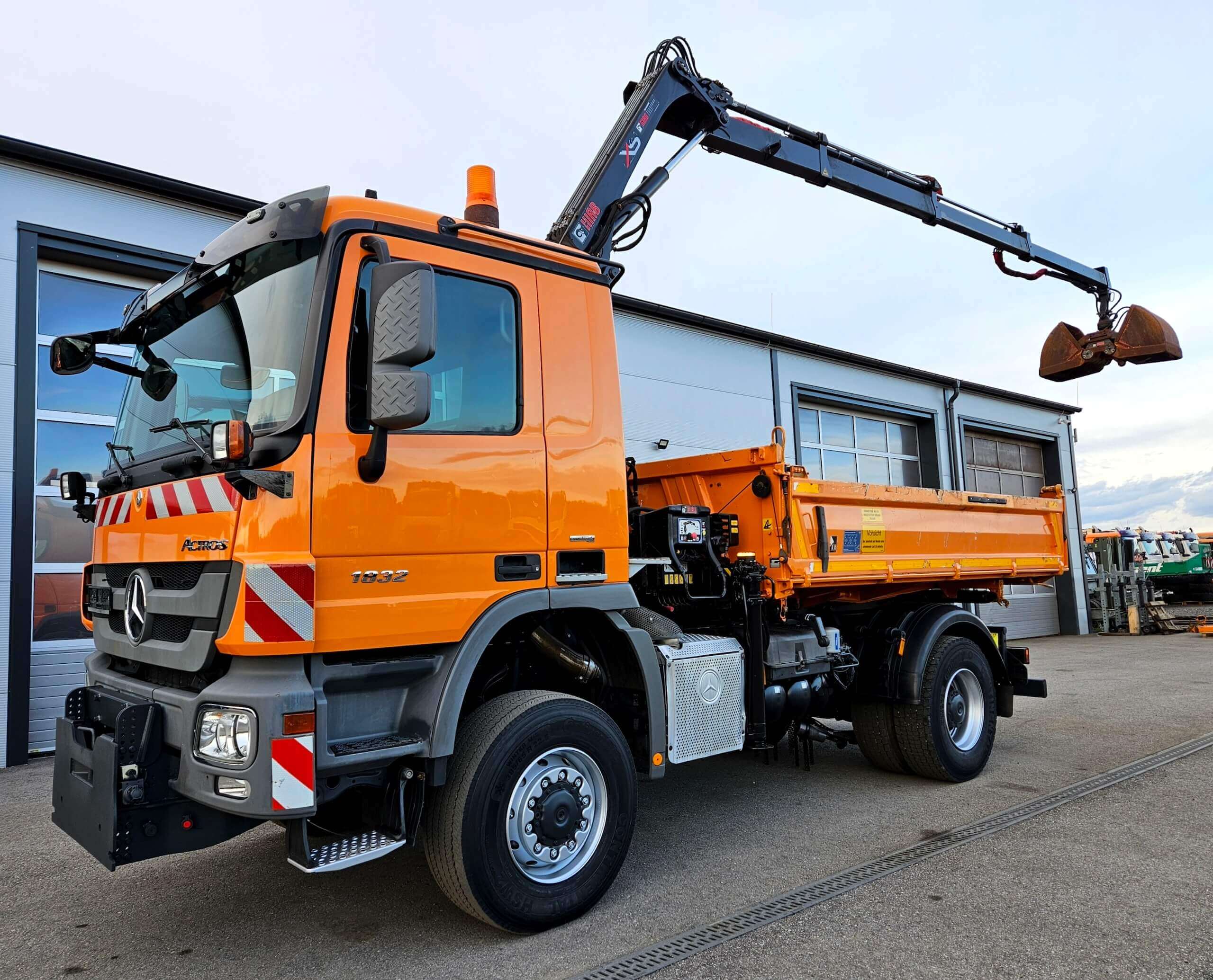 Orange Lkw mit Kran und Ladefläche vor einer Garage, ideal für Bau- und Transportdienste.