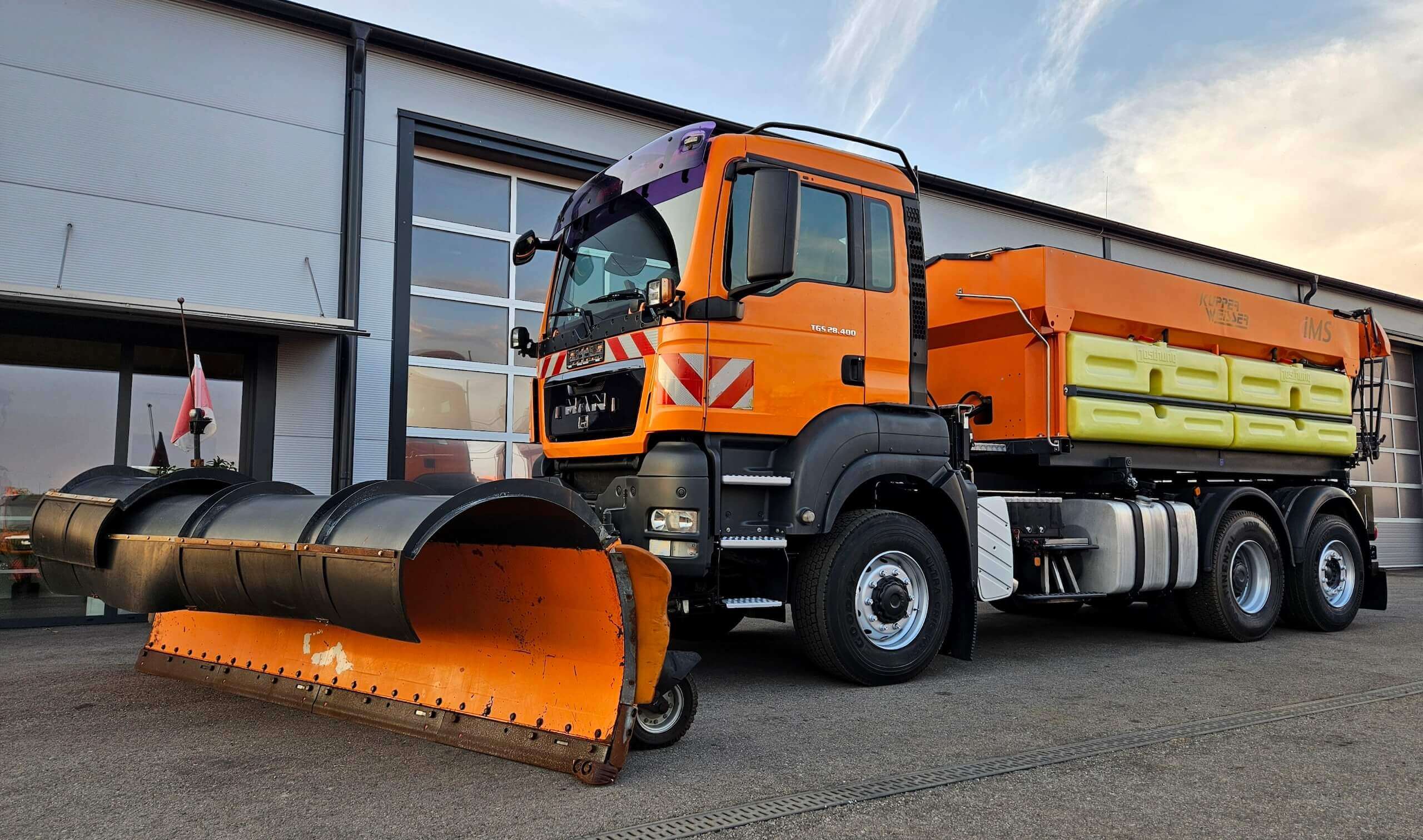 Orangefarbener Schneepflug-LKW parkt vor Garage, bereit für den Winterdienst.